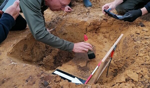 Voorzichtig legt een archeoloog het spoor van een paal bloot waarin munten zaten.
